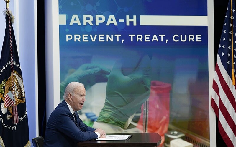 Biden, seated and in profile, in front of a backdrop that reads "ARPA-H: Prevent, treat, cure"